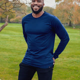 A tall athletic guy wearing a long sleeve navy tall t-shirt and smiling in a park with hands behind back.