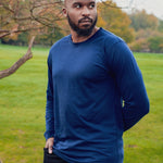 A tall athletic guy wearing a long sleeve navy tall t-shirt in a park with one hand in pocket.