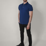 A head to toe shot of a tall skinny guy wearing an XL tall navy pique polo shirt, right hand in pocket.