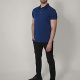 A head to toe shot of a tall skinny guy wearing an XL tall navy pique polo shirt, right hand in pocket.