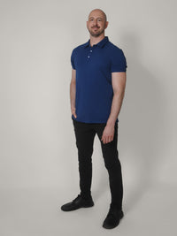 Thumbnail for A head to toe shot of a tall skinny guy wearing an XL tall navy pique polo shirt, right hand in pocket.