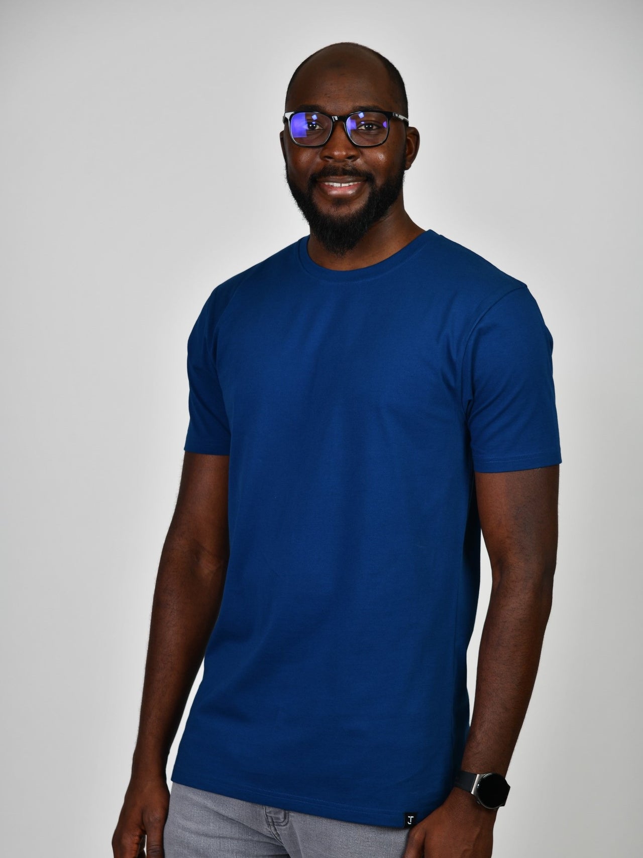 A tall and slim guy smiling in the studio and wearing a navy blue L tall slim t-shirt.