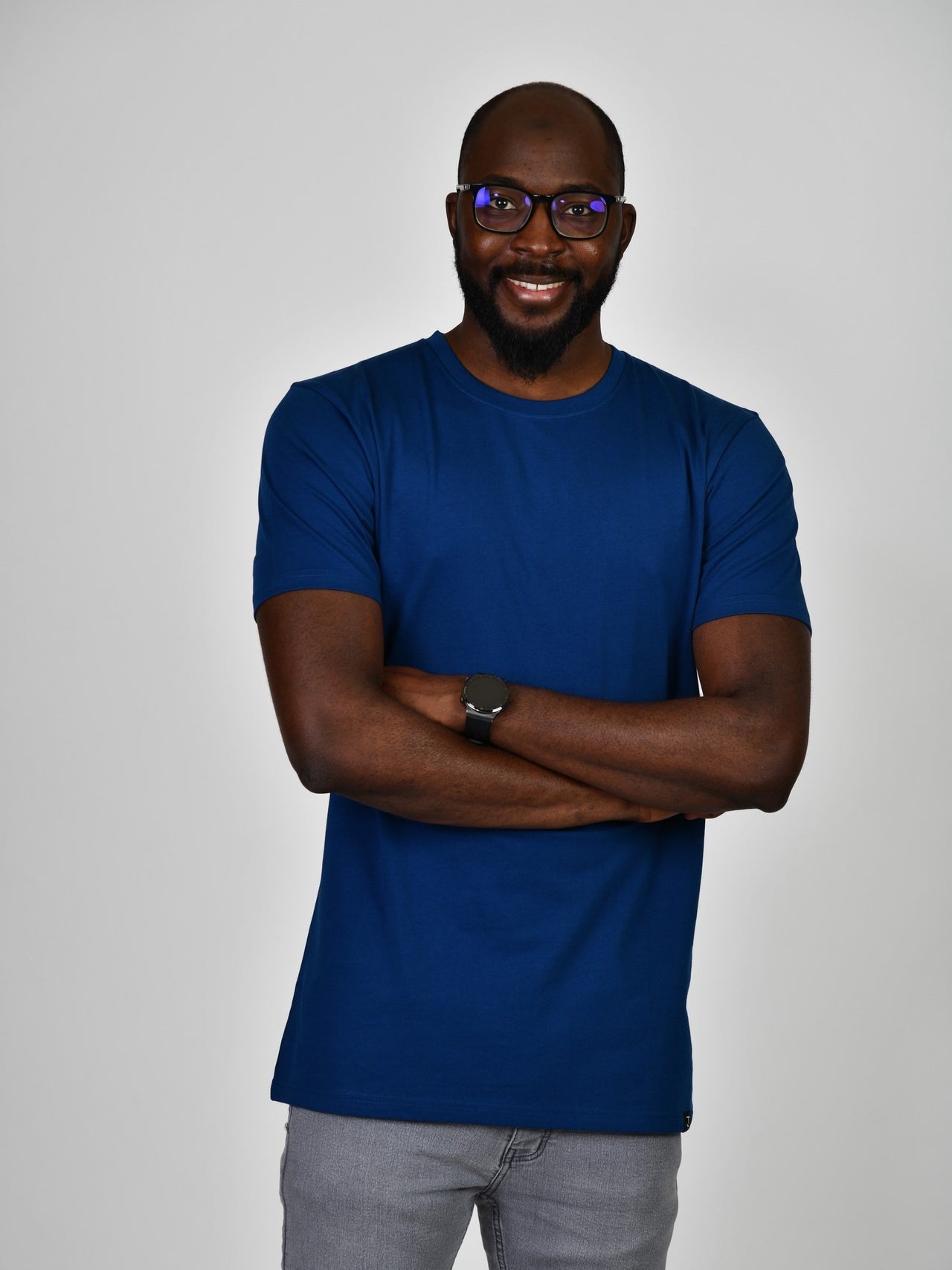A tall and slim guy in the studio, hands folded and wearing a navy blue L tall slim t-shirt.