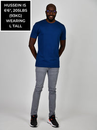 Thumbnail for A head to toe shot of a tall and slim guy in the studio, hands behind back, wearing a navy blue L tall slim t-shirt.