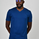 A tall and slim guy in the studio, hands behind back and wearing a navy blue L tall slim v-neck t-shirt.