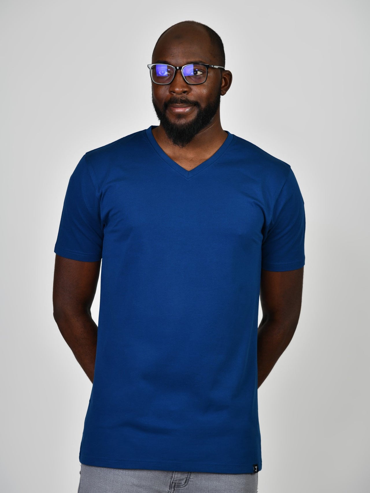 A tall and slim guy in the studio, hands behind back and wearing a navy blue L tall slim v-neck t-shirt.