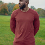 A shot of a tall athletic guy in a park wearing a dark orange long sleeve tall t-shirt, looking to the right.