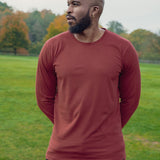 A shot of a tall athletic guy in a park wearing a dark orange long sleeve tall t-shirt, looking to the right.