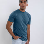 An upper body shot of a tall skinny guy wearing a petrol medium tall t-shirt, hand in pocket.