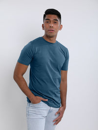 Thumbnail for An upper body shot of a tall skinny guy wearing a petrol medium tall t-shirt, hand in pocket.