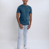 A head to toe shot of a tall skinny guy wearing a petrol medium tall t-shirt and smiling.