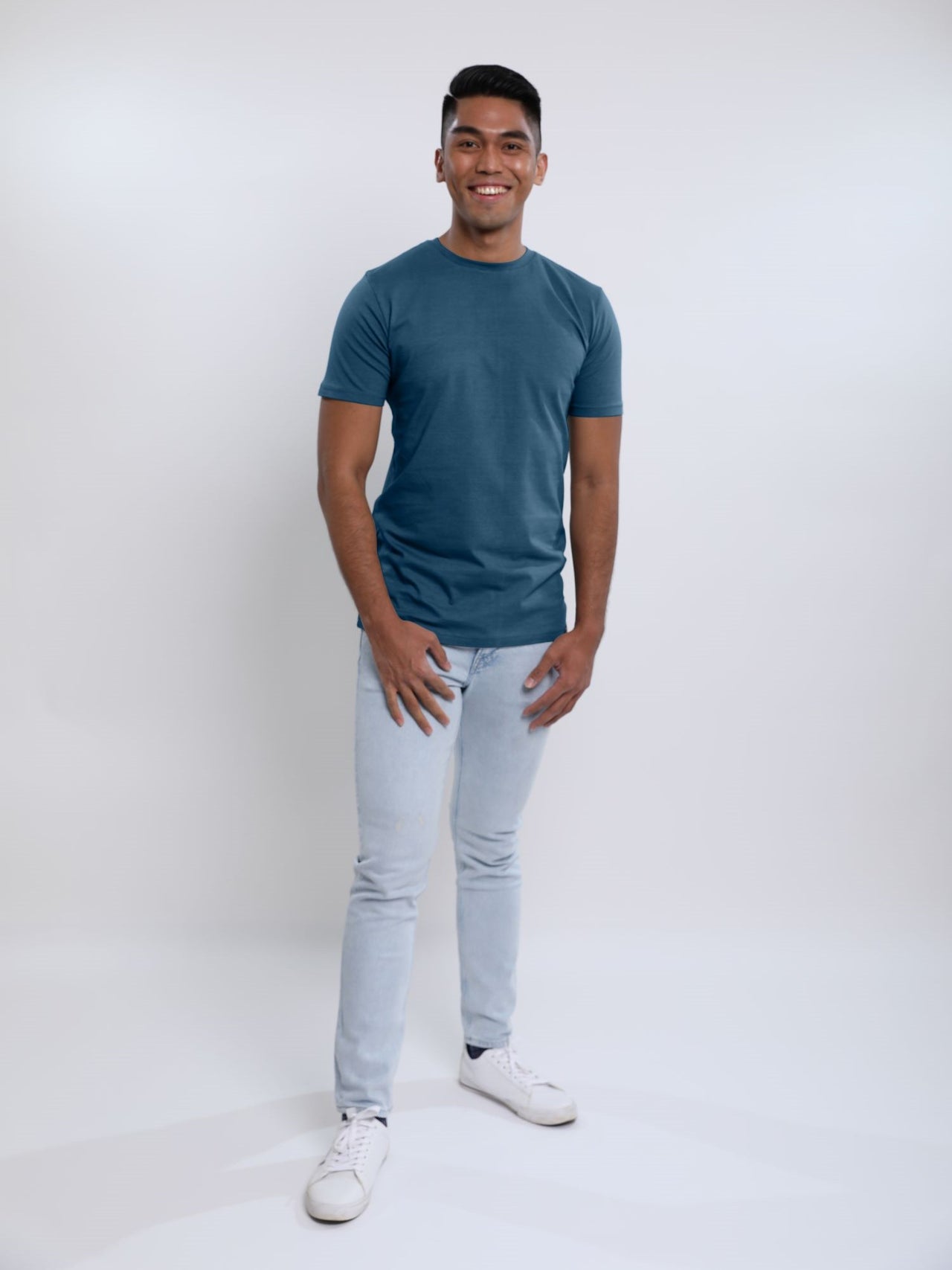 A head to toe shot of a tall skinny guy wearing a petrol medium tall t-shirt and smiling.