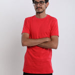 A tall skinny guy in the studio with his arms folded and wearing a red small tall slim t-shirt.