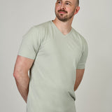 A tall and slim guy in the studio, hands behind back and wearing a sage green XL tall slim v-neck t-shirt.