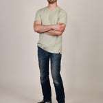 A head to toe shot of a tall and slim guy in the studio, hands folded and wearing a sage green XL tall slim v-neck t-shirt.