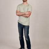 A head to toe shot of a tall and slim guy in the studio, hands folded and wearing a sage green XL tall slim v-neck t-shirt.