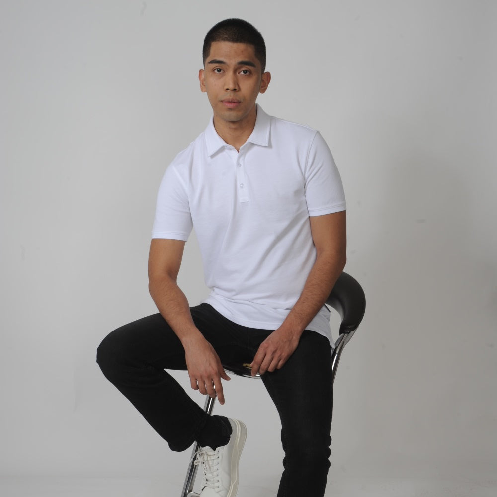A tall skinny guy sitting on a stool and wearing a white tall slim polo shirt.