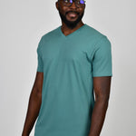 A tall and slim guy smiling in the studio and wearing a teal L tall slim v-neck t-shirt.