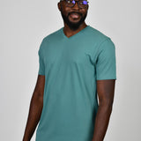 A tall and slim guy smiling in the studio and wearing a teal L tall slim v-neck t-shirt.