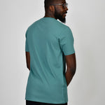 A shot from behind of a tall and slim guy in the studio and wearing a teal L tall slim v-neck t-shirt.