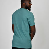 A shot from behind of a tall and slim guy in the studio and wearing a teal L tall slim v-neck t-shirt.