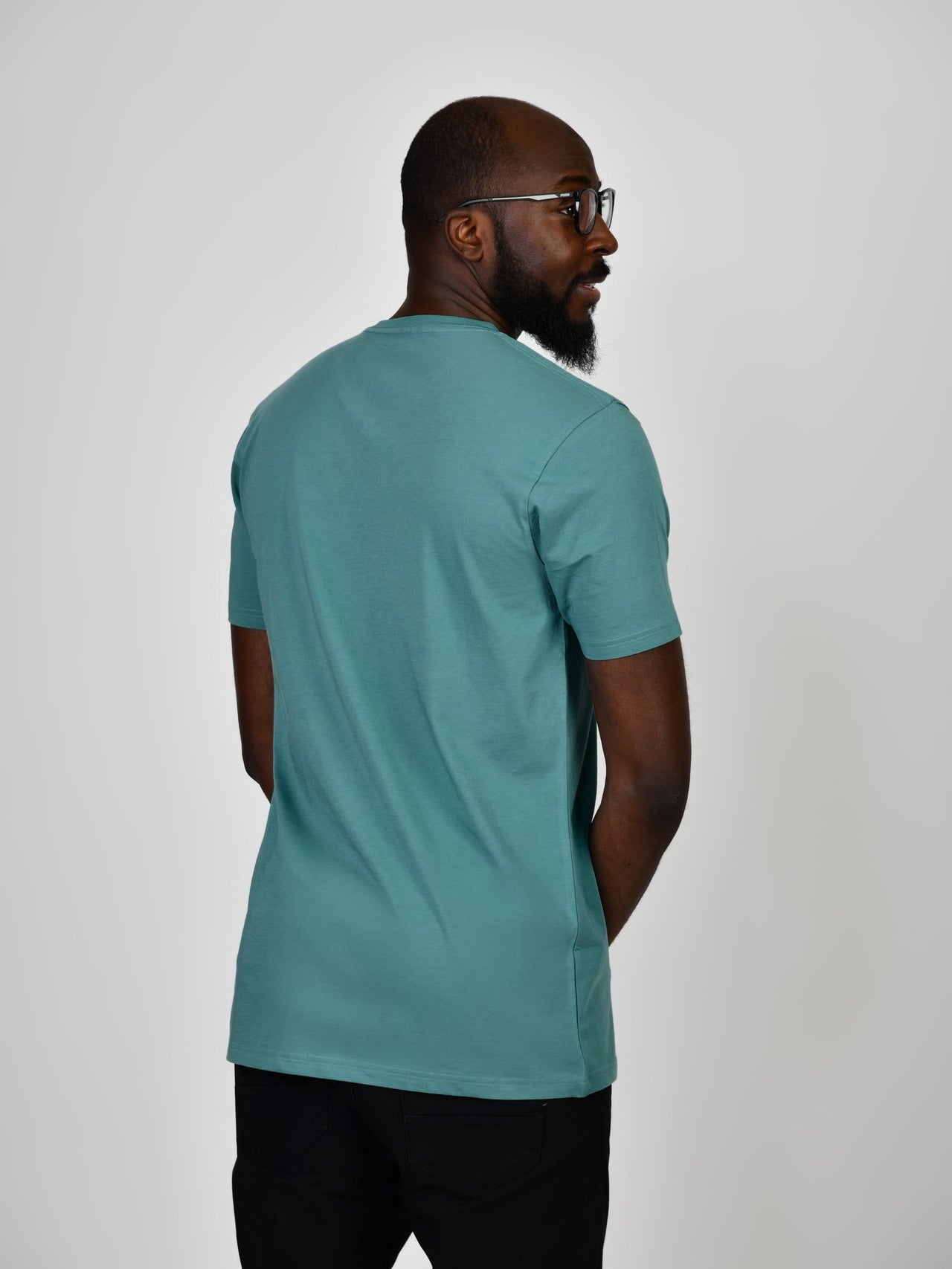 A shot from behind of a tall and slim guy in the studio and wearing a teal L tall slim v-neck t-shirt.