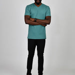 A head to toe shot of a tall and slim guy in the studio, hands folded and wearing a teal L tall slim v-neck t-shirt.