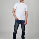 A head to toe shot of a tall and slim guy, hand in pocket, in the studio wearing a white XL tall slim t-shirt.