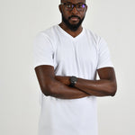 A tall and slim guy in the studio, hands folded and wearing a white L tall slim v-neck t-shirt.