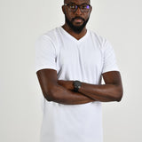 A tall and slim guy in the studio, hands folded and wearing a white L tall slim v-neck t-shirt.