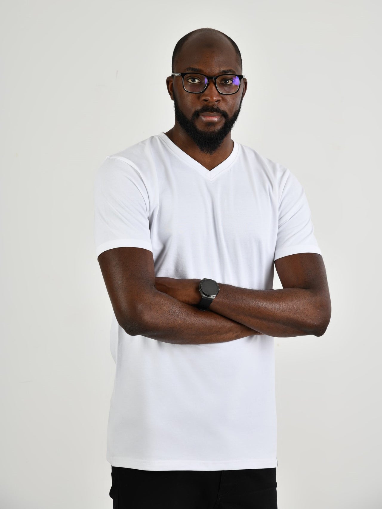 A tall and slim guy in the studio, hands folded and wearing a white L tall slim v-neck t-shirt.