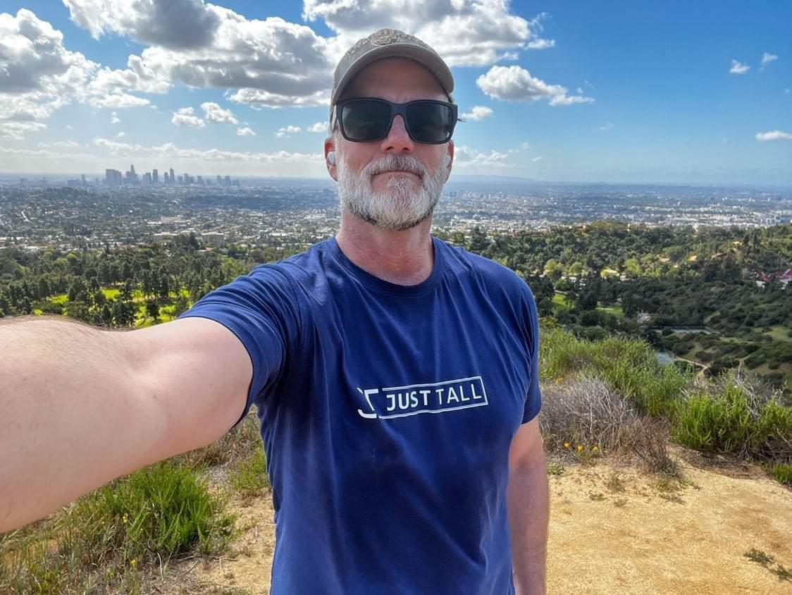 A tall athletic guy wearing an XL tall navy graphic t-shirt.